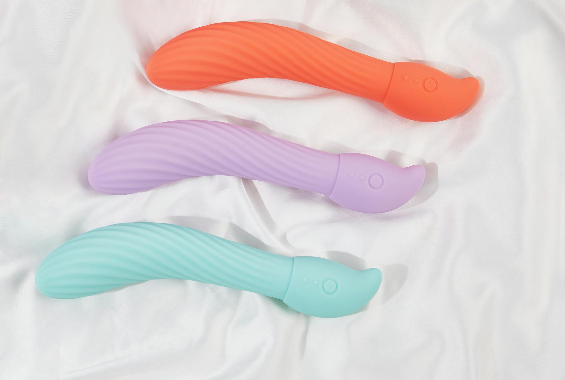 Three colorful clitoral vibrators arranged on white fabric, highlighting their smooth texture.