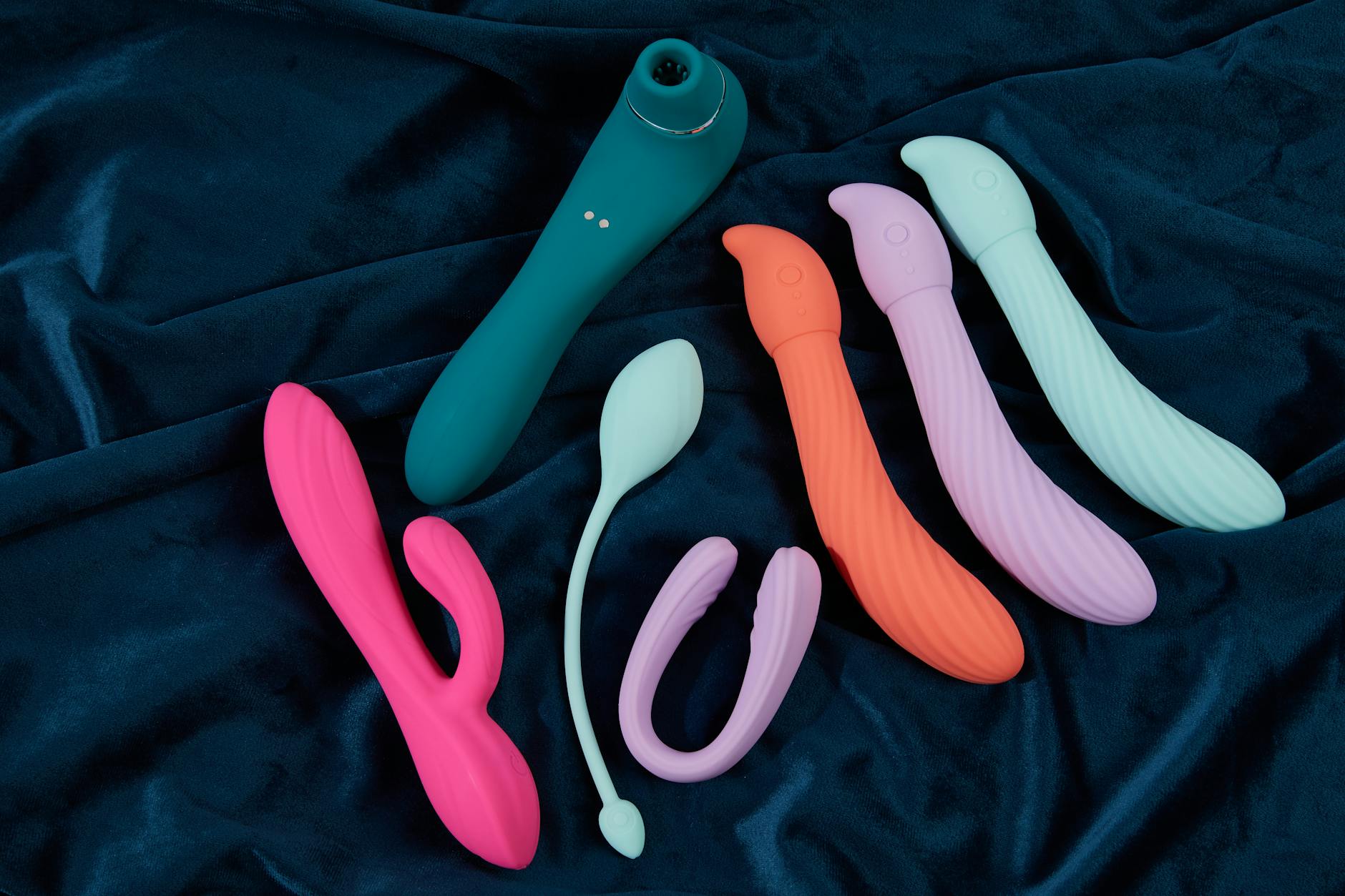 Collezione di vibratori colorati su tessuto blu scuro, mostrando forme e texture diverse