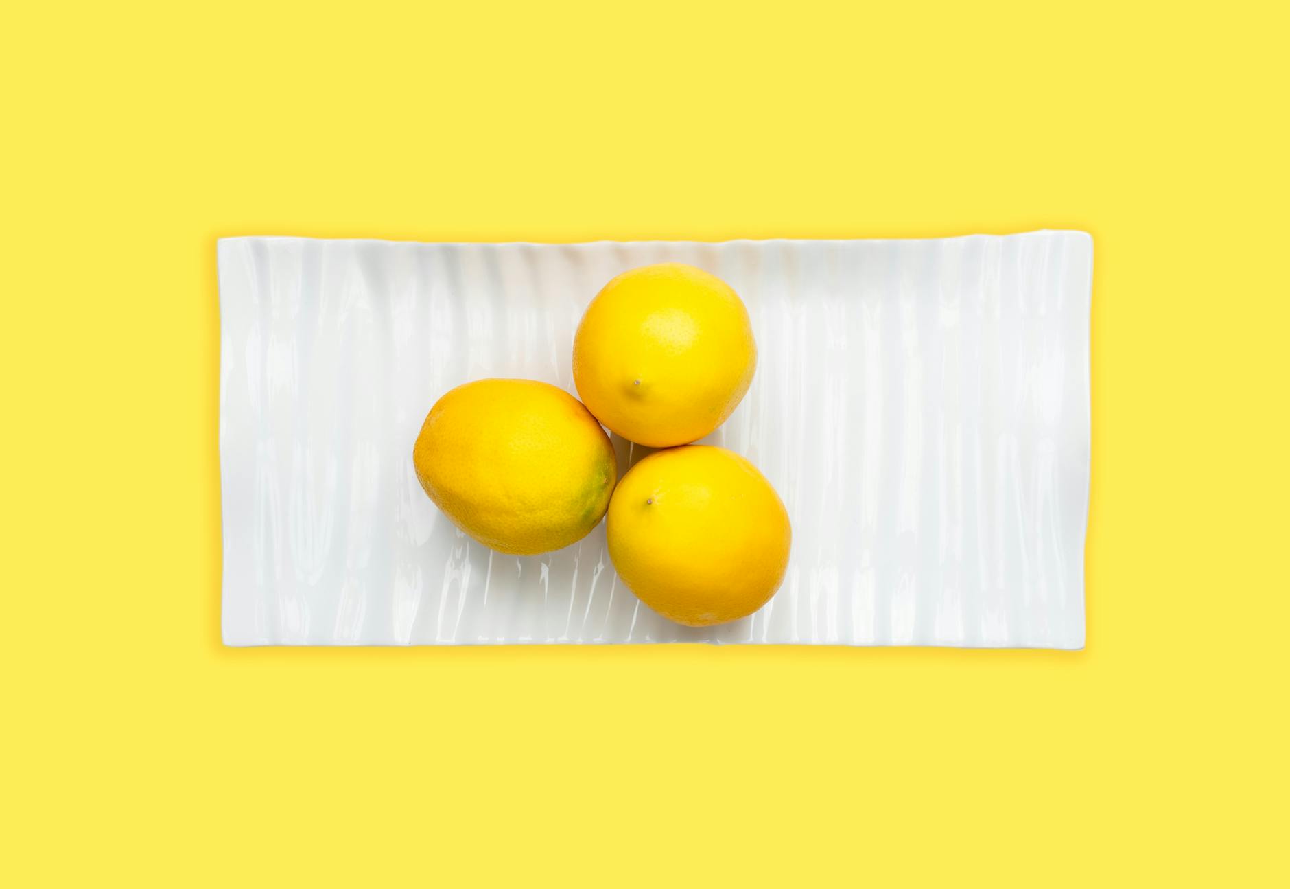 Fresh lemons on a white plate with a vibrant yellow background, symbolizing natural vitality and renewal
