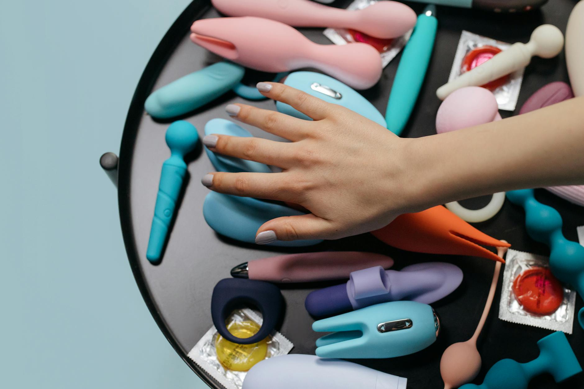 Una mano che si estende verso una varietà di vibratori colorati disposti su un tavolo