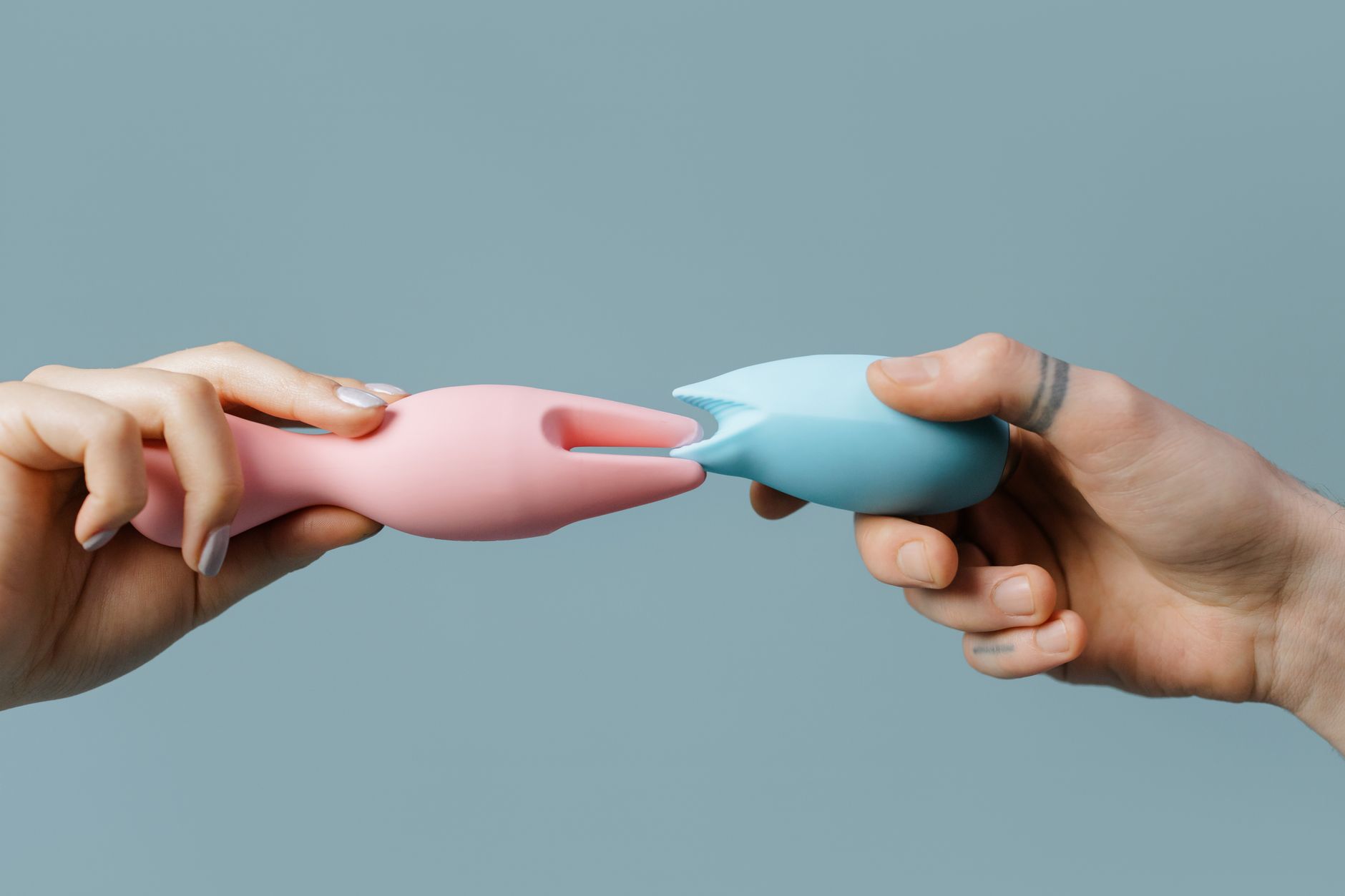 A woman in glasses holds two colorful vibrators against a purple background, representing the confidence that comes with exploring pleasure intentionally.
