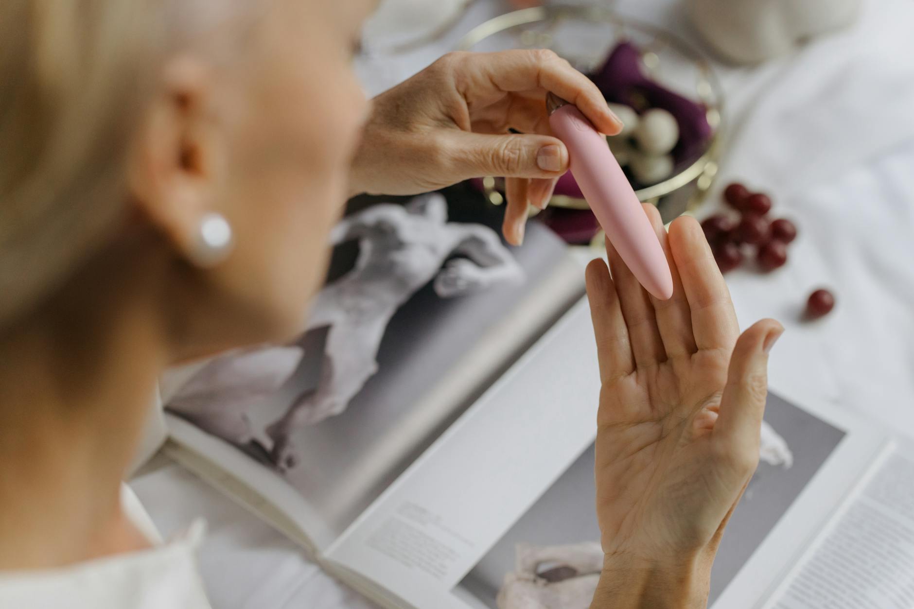 Close-up of a hand holding a pink vibrator next to art books on a white surface