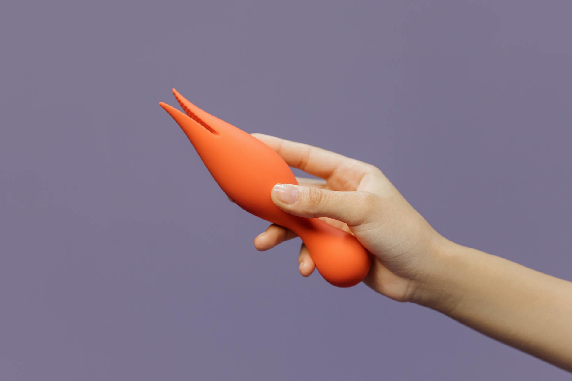 A hand holding a lemon clitoral vibrator against a minimalistic purple backdrop, symbolizing modern partnered pleasure
