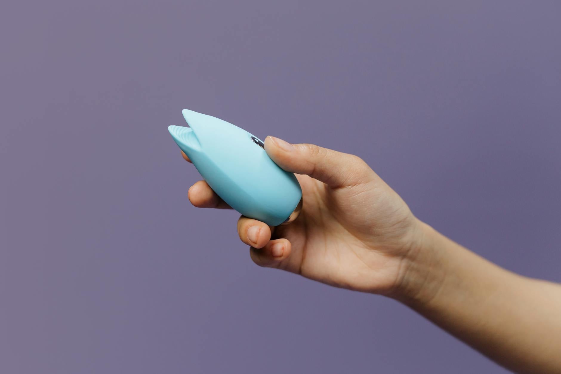 Un vibratore in silicone blu tenuto in mano su sfondo viola, che promuove l'amore per sé stessi e la sessualità consapevole