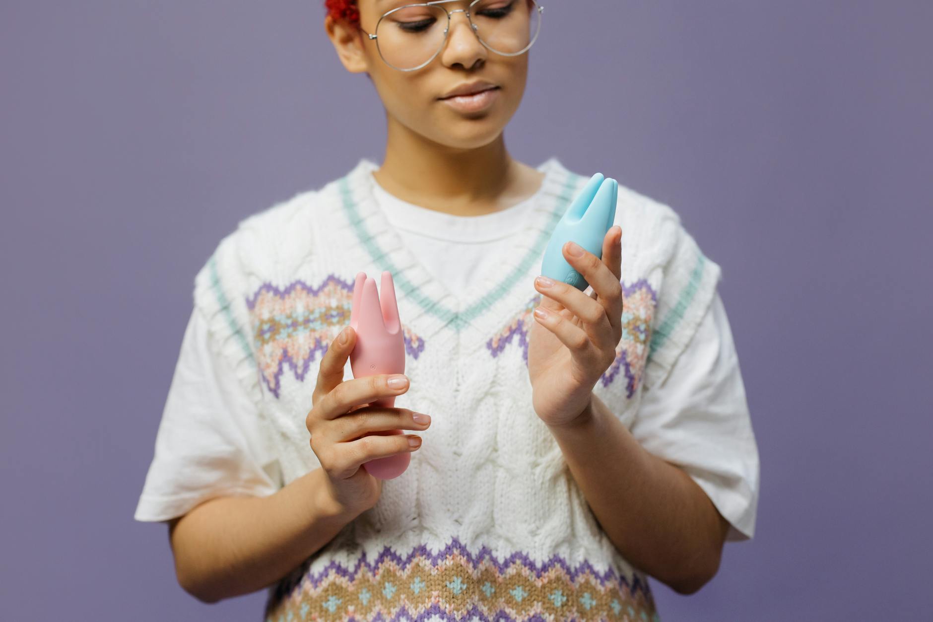 Woman holding blue and pink vibrators in thoughtful contemplation about intimacy