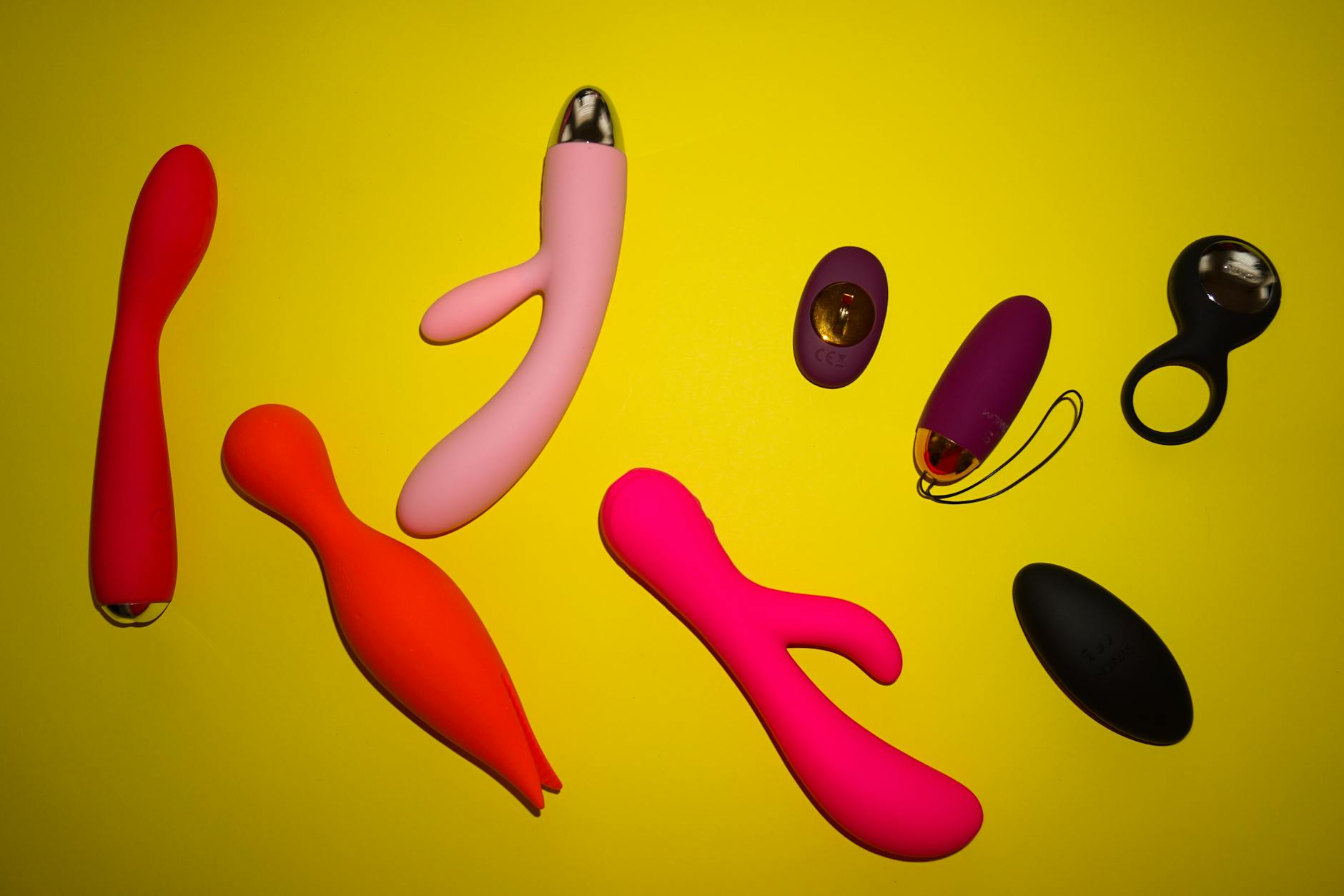Colorful sex toys arranged on a bright yellow surface showcasing diverse adult toy options