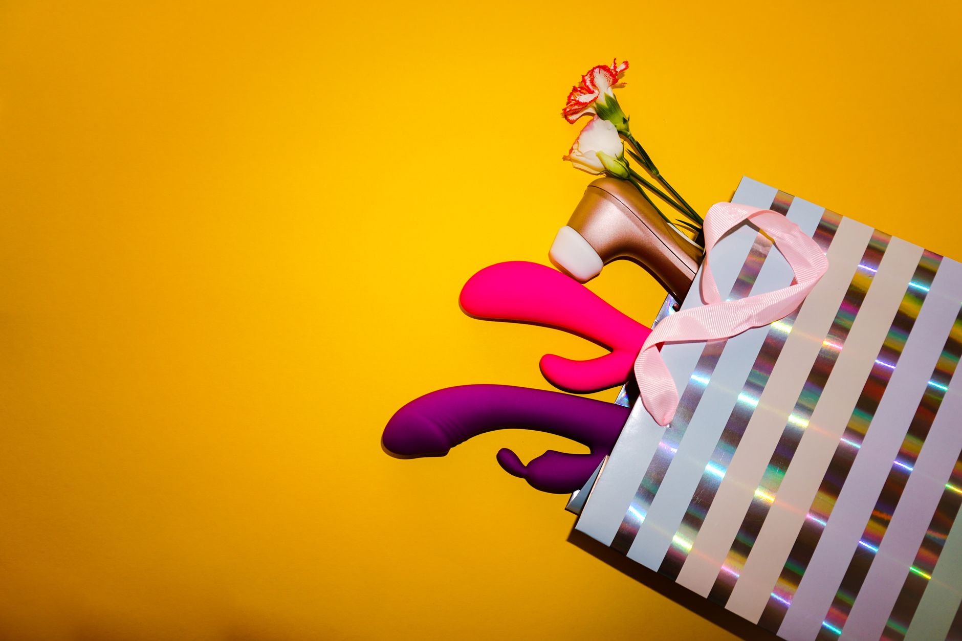 Colorful vibrators arranged on a bright yellow background in a holographic gift bag